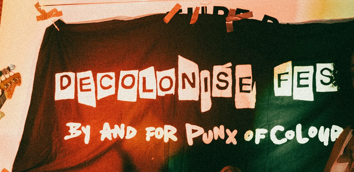 Decolonise Fest Banner. Black with white logo text hanging on wall at one of the fests