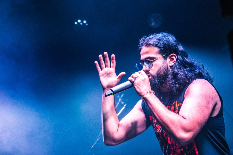 Hyphen singing onstage with hand up and smoke in background