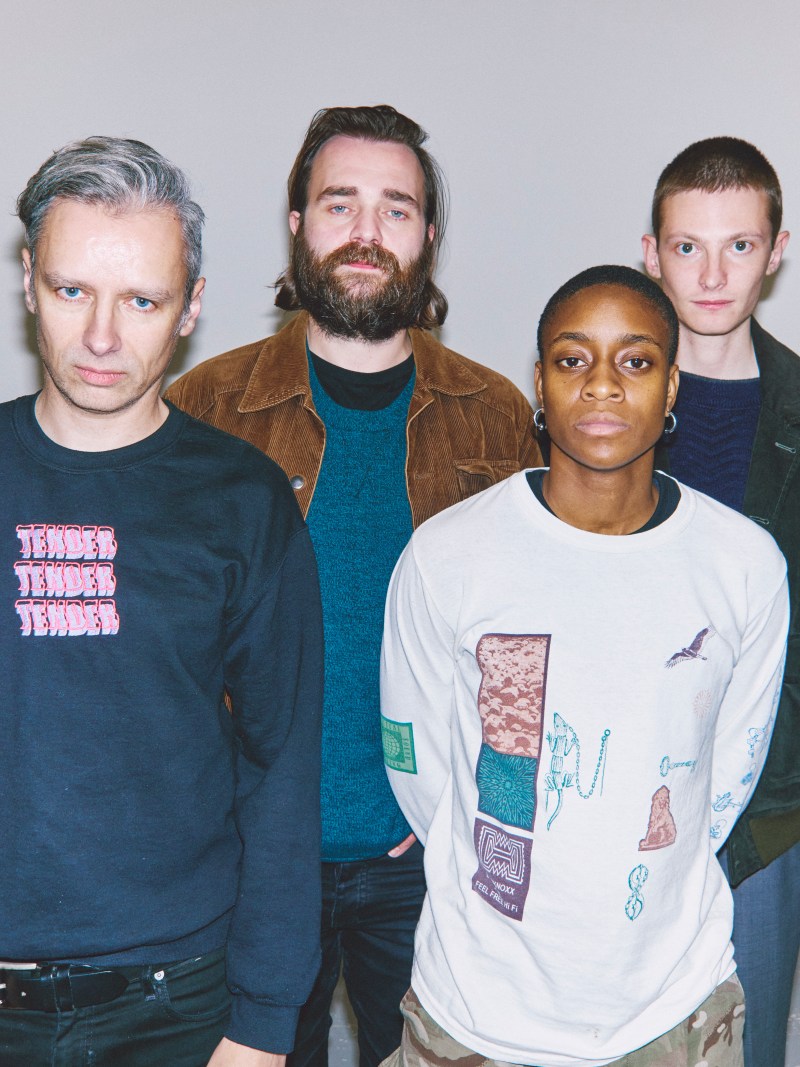 The None 4 piece band standing against grey wall